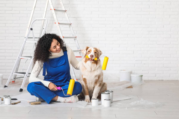 Woman in overalls sitting on the ground with a dog, both holding various painting nap lengths at Triboro Paint near North Attleborough, MA