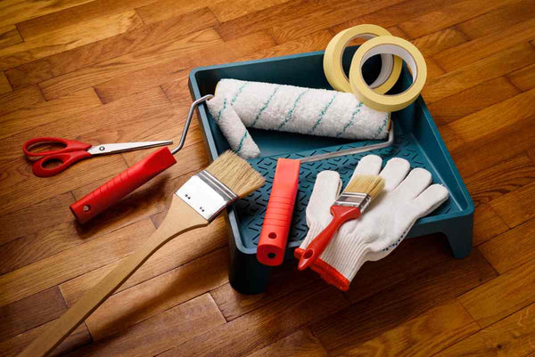 Various painting tools, including painter's tape, brushes, and rollers, laid out on a hardwood floor at Triboro Paint near North Attleborough, MA