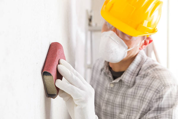 Person wearing safety gear, like a mask, and using sanding products on his wall before painting