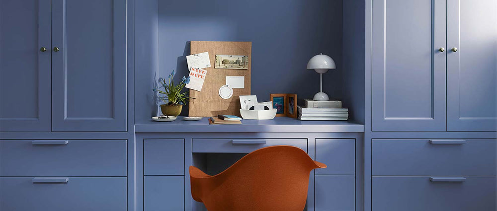 A modern red office chair sits in a home office painted in Blue Nova 825, with built-in shelving, cabinetry and in-set desk topped with a pegboard, plants, books and a modern domed white desk lamp.